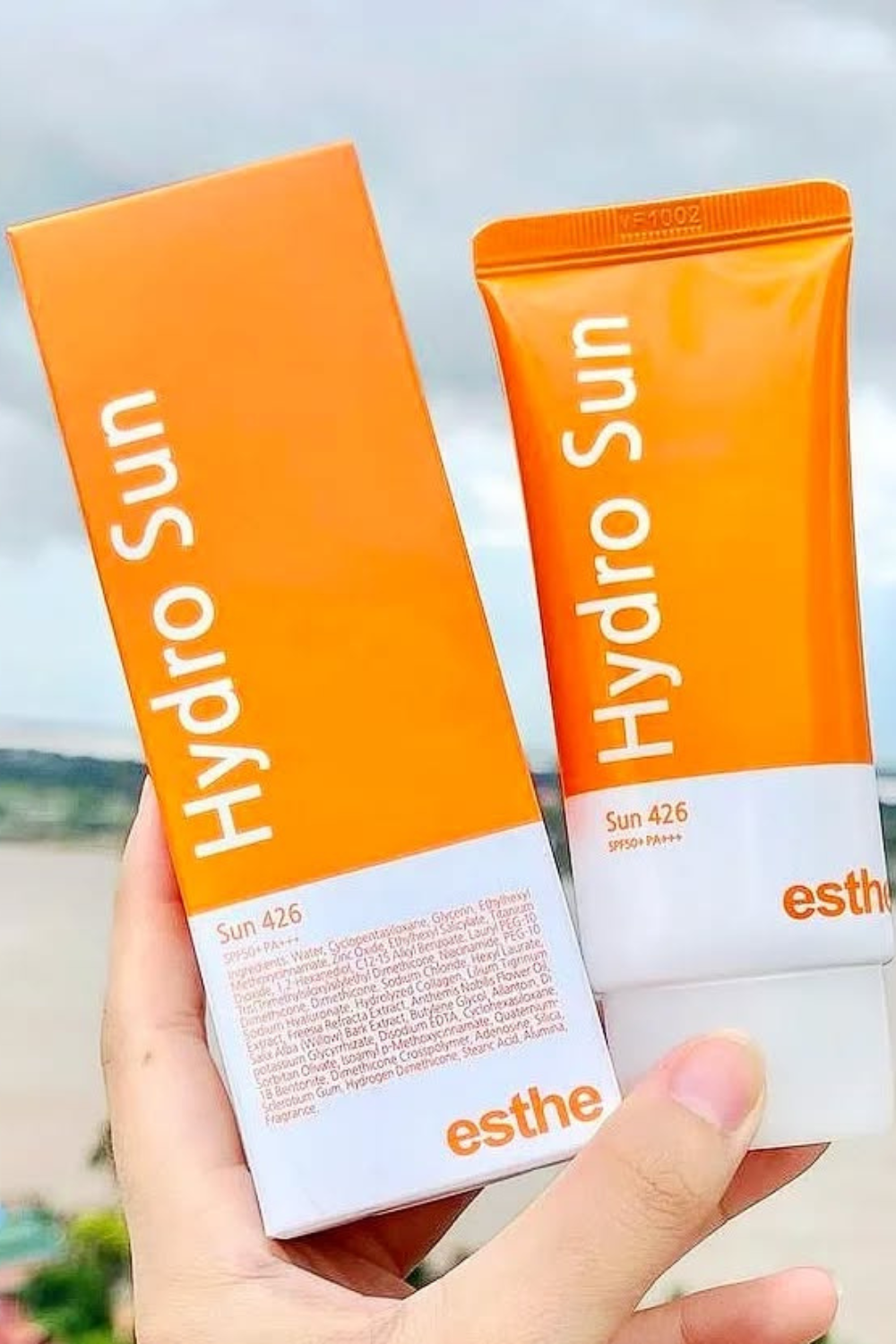 Hand holding Hydro Sun SPF50+ PA+++ sunscreen tube and box against a blurred outdoor background.
