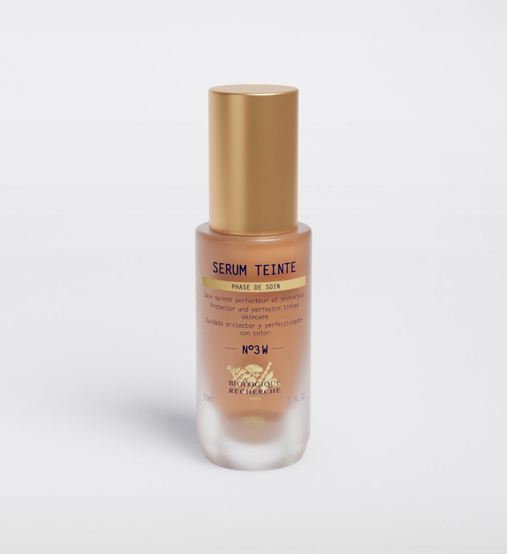 The Biologique Recherche Serum Teinte N3 Warm, featuring a gold cap and clear glass body, stands against a plain white background, offering hydrating action and a healthy glow for radiant skin.
