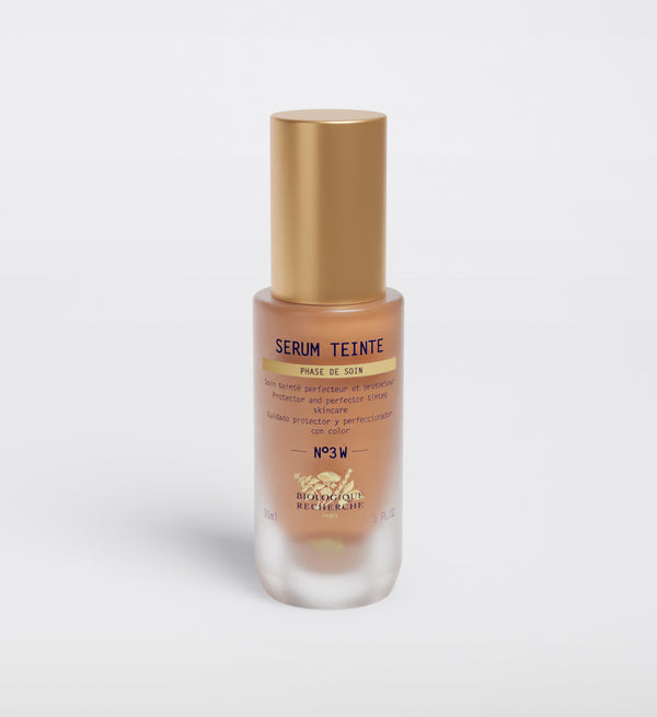 The Biologique Recherche Serum Teinte N3 Warm, featuring a gold cap and clear glass body, stands against a plain white background, offering hydrating action and a healthy glow for radiant skin.