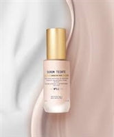 The Biologique Recherche Serum Teinte N1 Cold, featuring a gold cap, stands against a flowing white and beige background, promising a healthy glow effect.