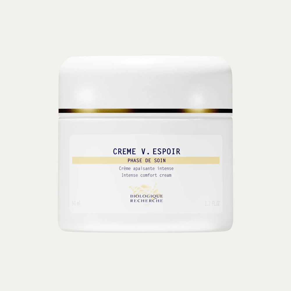 A white jar of Crème V. Espoir with gold detailing, described as an intense comfort cream formulated to calm reactive skin and reduce redness for a more even complexion.
