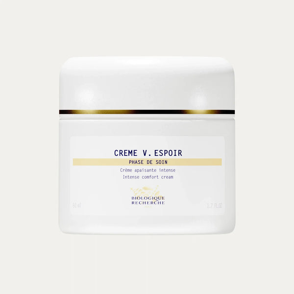 A white jar of Crème V. Espoir with gold detailing, described as an intense comfort cream formulated to calm reactive skin and reduce redness for a more even complexion.