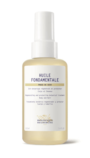 The transparent bottle of Huile Fondamentale showcases a regenerating, protective botanical treatment enriched with vegetable oils. Its multilingual label (French, English, Spanish) details its effectiveness in addressing skin and hair dryness.